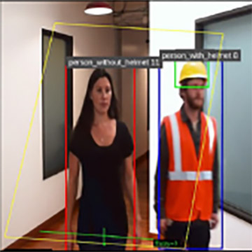 Foto einer Personenerkennung in einem Innenraum. Zwei Personen gehen durch einen Flur. Um die Personen sind farbige Begrenzungsrahmen und Beschriftungen eingeblendet, die eine automatische Erkennung durch ein Computer-Vision-System darstellen. Die linke Person trägt keinen Helm, was das Programm durch den Schirftzug person_without_helmet zeigt. Die rechte Person trägt Warnweste und Helm, und über ihr ist der Schriftzug person_with_helmet abgebildet.